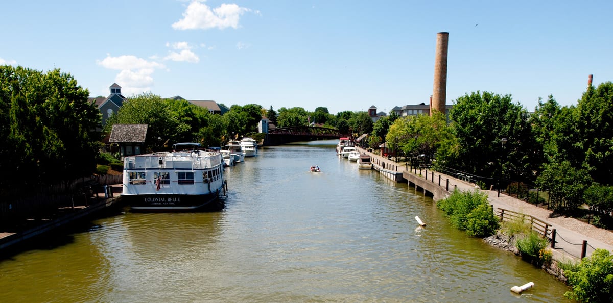 Colonial Belle tour boat moored on the Erie Canal in Fairport, a kayaker on the water and a landscaped towpath on the right leading to the lift bridge